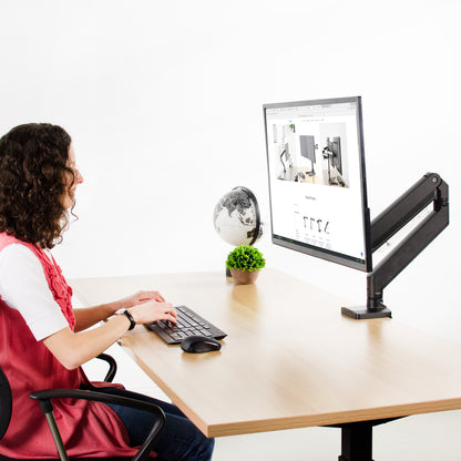  A person working at an ergonomic desk and LCD screen mounted to a monitor mount with steel adapter brackets.