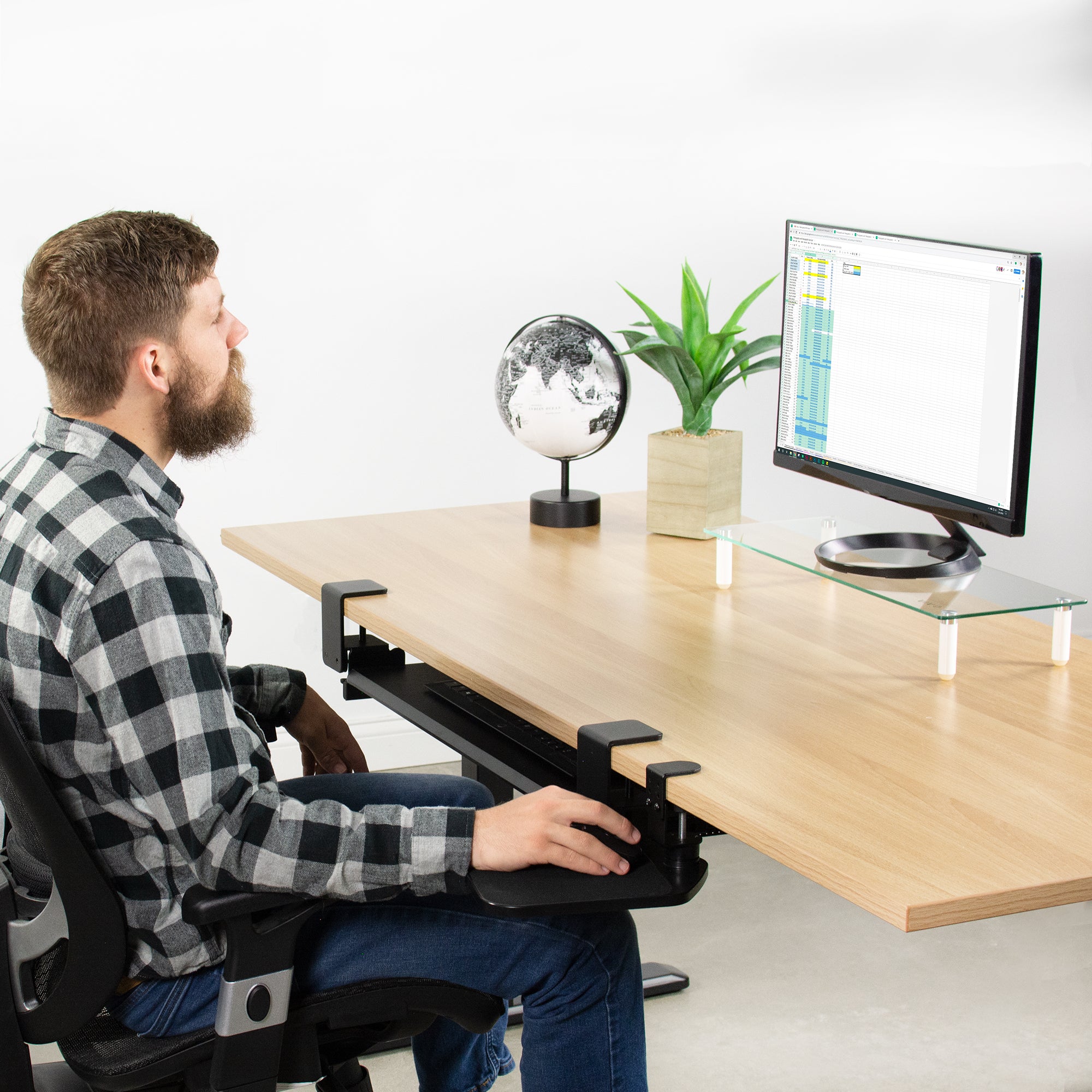 A man working at a desk while utilizing a clamp-on mouse pad.